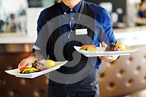 Waiter carrying two plates with meat dish on some festive event
