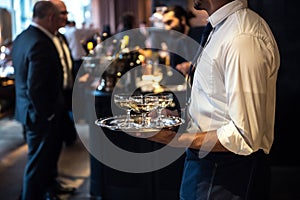 Waiter from catering service carrying champagne wine drinks on the event.