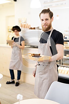 Waiter of coffee house carrying tray with cup