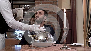 Waiter corrects placement of the glass and opens cloche showing the dish.