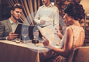 Waiter explaining the menu to wealthy couple in restaurant.