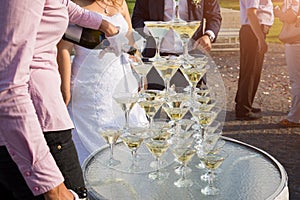 Waiter filling a pyramid of glasses with champagne at outdoor garden in wedding ceremony.