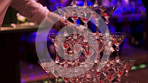 Waiter hand with glass of champagne over pyramid during catering at party. Clip. Pyramid of glasses of champagne