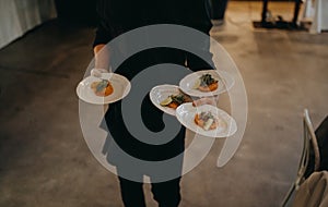 Waiter holding four plates with food in restaurant. Catering, service at the wedding reception. Salmon tartare as