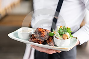 The waiter is holding a plate chicken wings grill. Barbecue restaurant menu, a series of photos of different meats