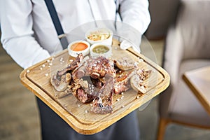 The waiter is holding a plate Various grilled meat set with Pickled cabbage and two sauces. Serving on a wooden Board