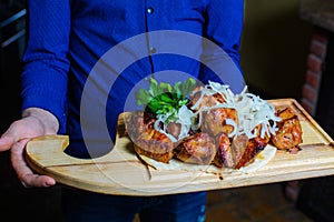 The waiter holds fried meat on a wooden board. Serving barbecue with herbs