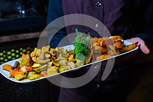 The waiter holds fried vegetables on a wooden board