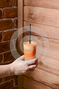 A waiter holds a glass of orange juice. Cup of juice with a straw in waiter hands at cafe. Wooden background