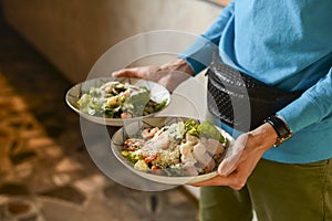 Waiter holds two plates with Italian salad with jamon, prosciutto, fresh vegetables and parmesan cheesein a restaurant