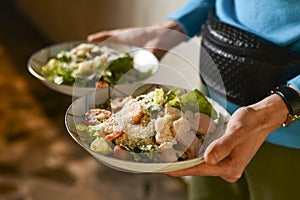 Waiter holds two plates with Italian salad with jamon, prosciutto, fresh vegetables and parmesan cheesein a restaurant