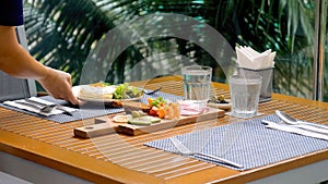 Waiter at a luxury outdoor tropical restaurant serves fresh, delicious food