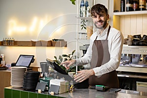 Waiter man working in coffee shop using terminal for checking orders standing at counter