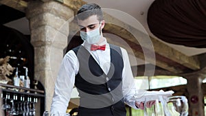 A waiter in a medical protective mask serves the table in the restaurant