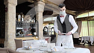 A waiter in a medical protective mask serves the table in the restaurant