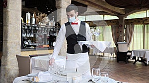 A waiter in a medical protective mask serves the table in the restaurant