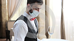 A waiter in a medical protective mask serves the table in the restaurant