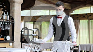 A waiter in a medical protective mask serves the table in the restaurant