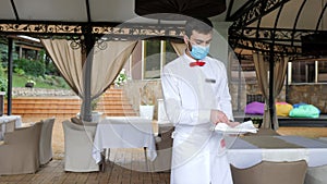 A waiter in a medical protective mask serves the table in the restaurant