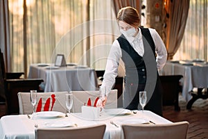 A waiter in a medical protective mask serves the table in the restaurant.