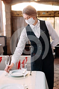 A waiter in a medical protective mask serves the table in the restaurant.