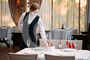 A waiter in a medical protective mask serves the table in the restaurant.