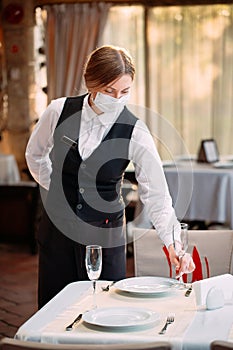 A waiter in a medical protective mask serves the table in the restaurant.