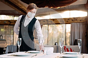 A waiter in a medical protective mask serves the table in the restaurant.
