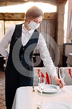 A waiter in a medical protective mask serves the table in the restaurant.