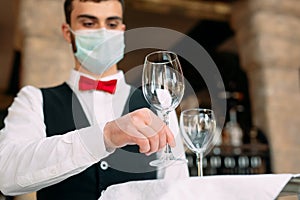 A waiter in a medical protective mask serves the table in the restaurant.