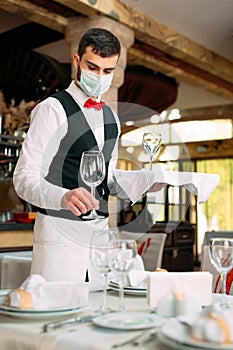 A waiter in a medical protective mask serves the table in the restaurant.