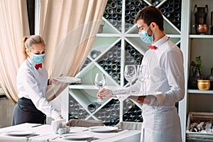 A waiter in a medical protective mask serves a table in the restaurant. Employees of a restaurant or hotel in protective