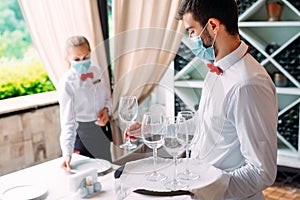 A waiter in a medical protective mask serves a table in the restaurant. Employees of a restaurant or hotel in protective