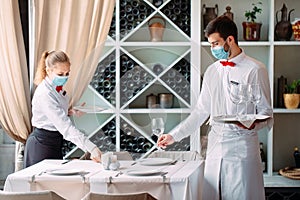 A waiter in a medical protective mask serves a table in the restaurant. Employees of a restaurant or hotel in protective