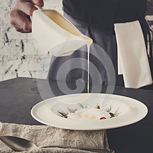 Waiter pouring broth to mushroom cream soup