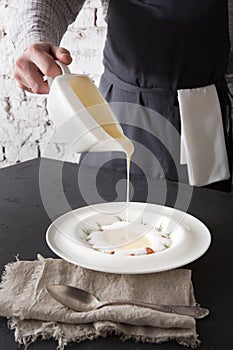 Waiter pouring broth to mushroom cream soup