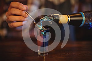 Waiter pouring cocktail drink into shot glasses at counter