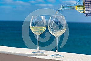 Waiter pouring glass of white wine on outdoor terrace with sea v