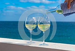 Waiter pouring glass of white wine on outdoor terrace with sea v