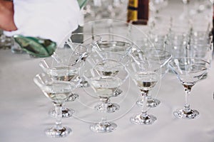 Waiter pouring martini in crystal glasses on table party at wedding reception. Martini row drinks at alcohol bar. Christmas and