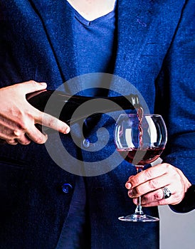 Waiter pouring red wine in a glas. Sommelier man, degustator, winery, male winemaker. Bottle, red wine glass. Pouring