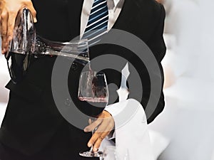 Waiter pouring red wine in a glass at a restaurant table