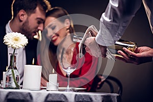 waiter pouring wine while beautiful couple having romantic date in restaurant