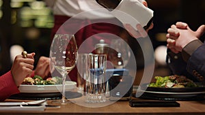 Waiter pouring wine glass at fine restaurant table. Couple enjoy fancy dining.