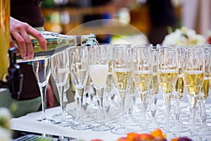 The waiter pours champagne into a glass.Empty glasses on the white table, A row of empty champagne