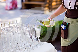 The waiter pours champagne into a glass.Empty glasses on the white table, A row of empty champagne