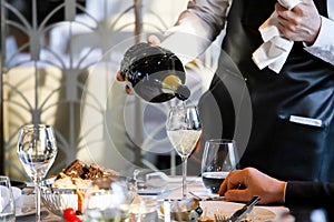 The waiter pours white wine into a glass. Banquet, cutlery, table setting. photo