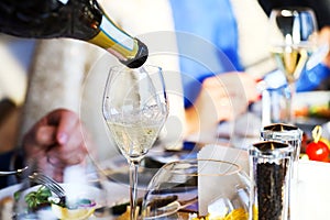 The waiter pours white wine into a glass. Banquet, cutlery, table setting. photo