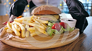 Waiter put on the table a french fries with burger on wooden board.