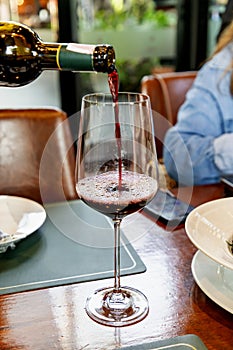 A waiter in a restaurant is pouring wine into wine glasses on a table at a party. There are blurry people attending the event in